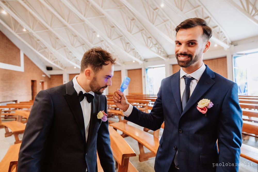Two groomsmen sharing a lighthearted moment in formal attire at a church.