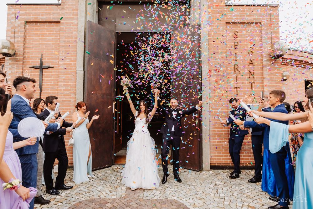 Wedding guests shower the newlyweds with confetti outside a brick church entrance.
