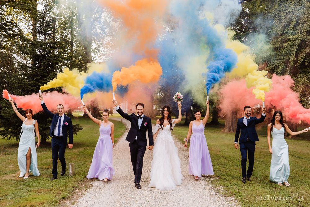 Wedding party celebrates with vibrant smoke bombs creating colorful clouds in an outdoor setting.