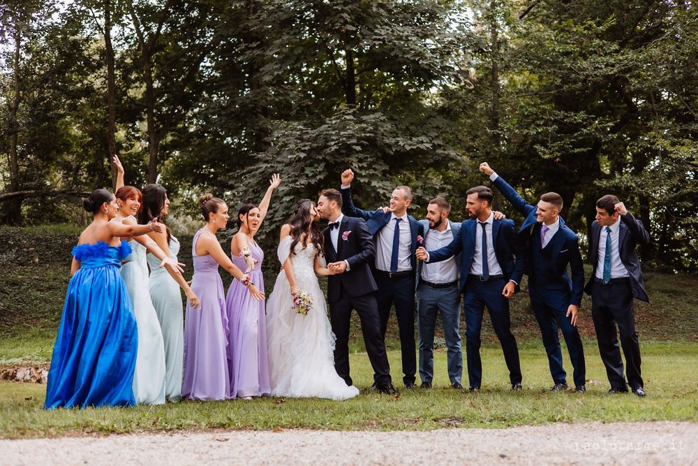 Wedding party poses together on a garden path wearing blue and purple formal attire.