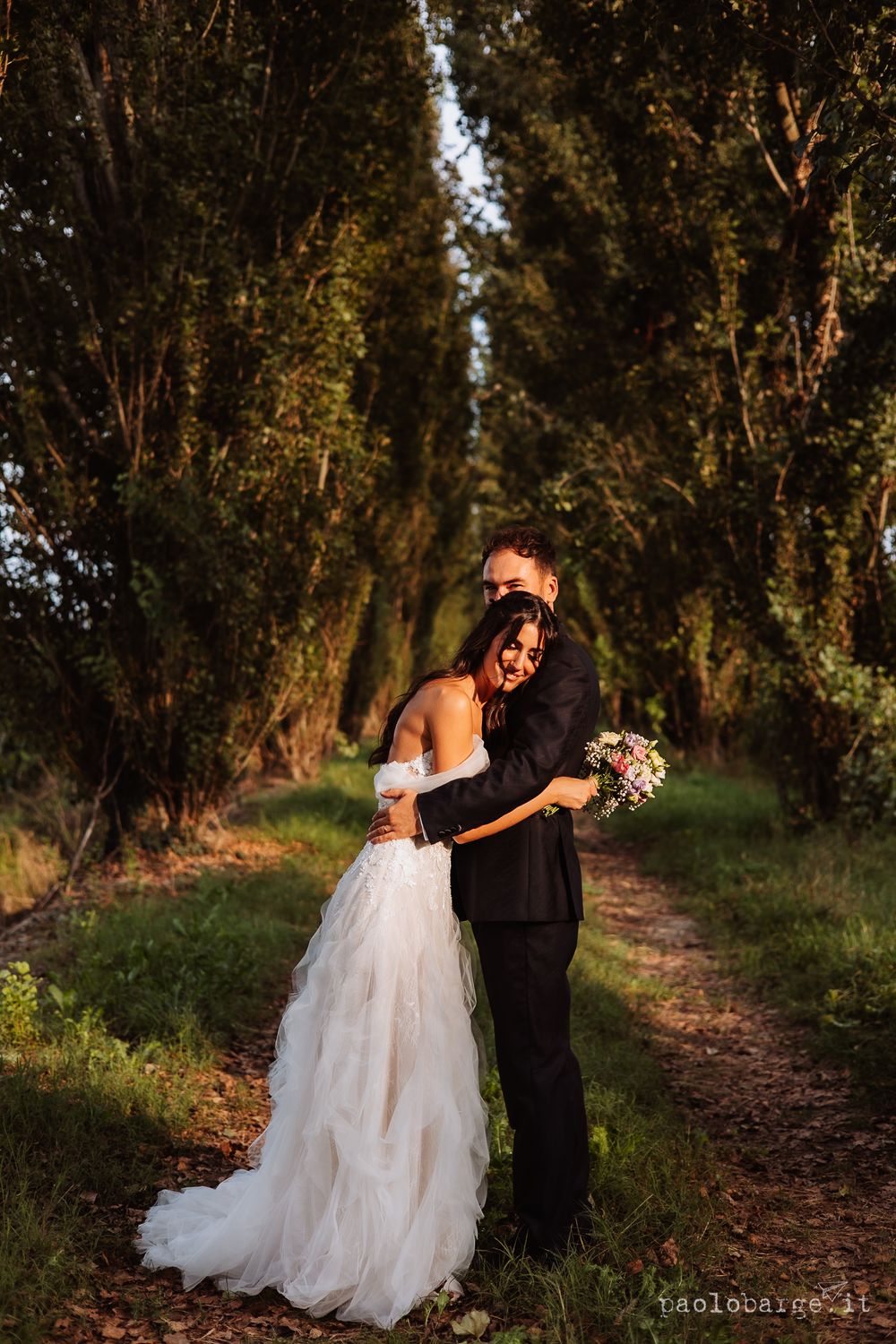 A romantic moment between newlyweds on a tree-lined path at sunset.