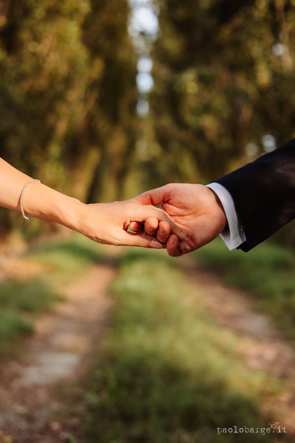 Close-up of bride and groom holding hands against a natural forest backdrop.