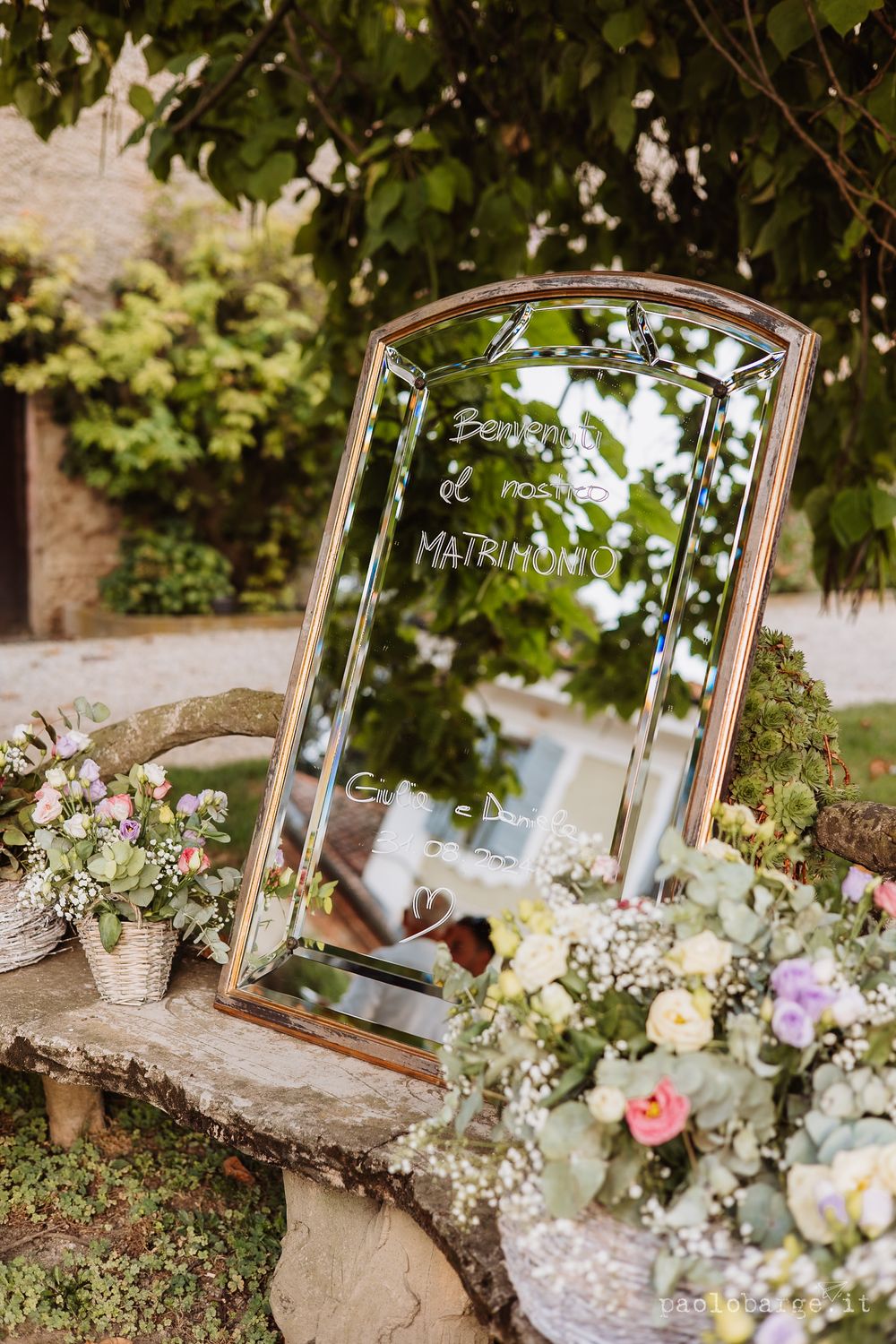 Decorative mirror with floral arrangements creates a romantic wedding display in a garden setting.