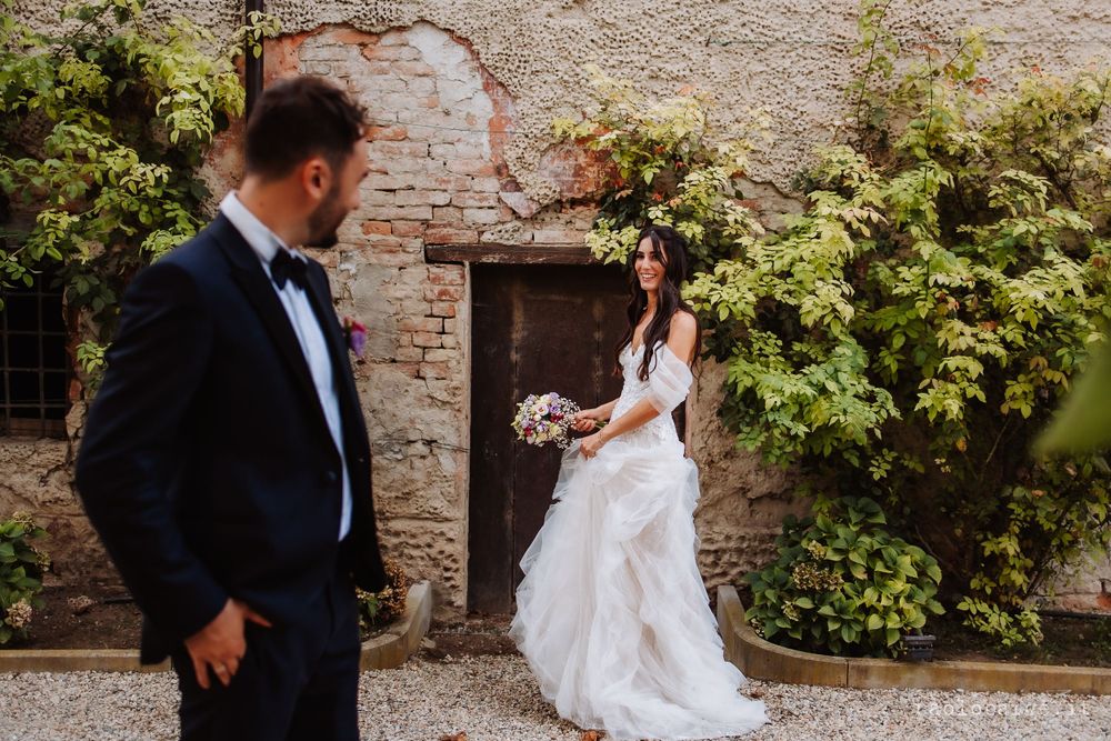 A wedding couple poses against rustic stone wall covered in lush green vines.
