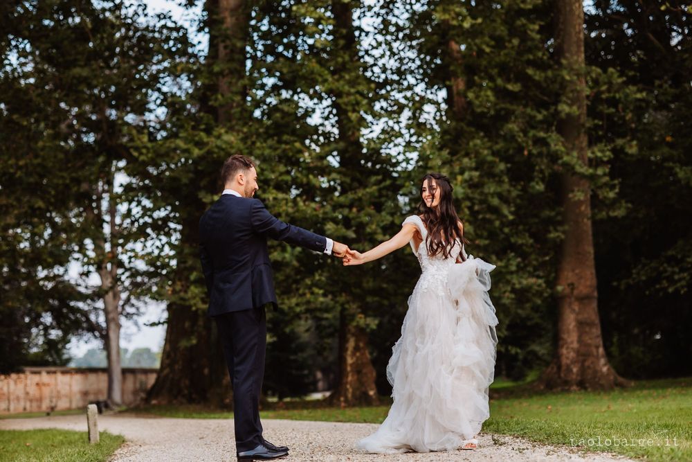 A couple twirls together on a garden path surrounded by tall trees.