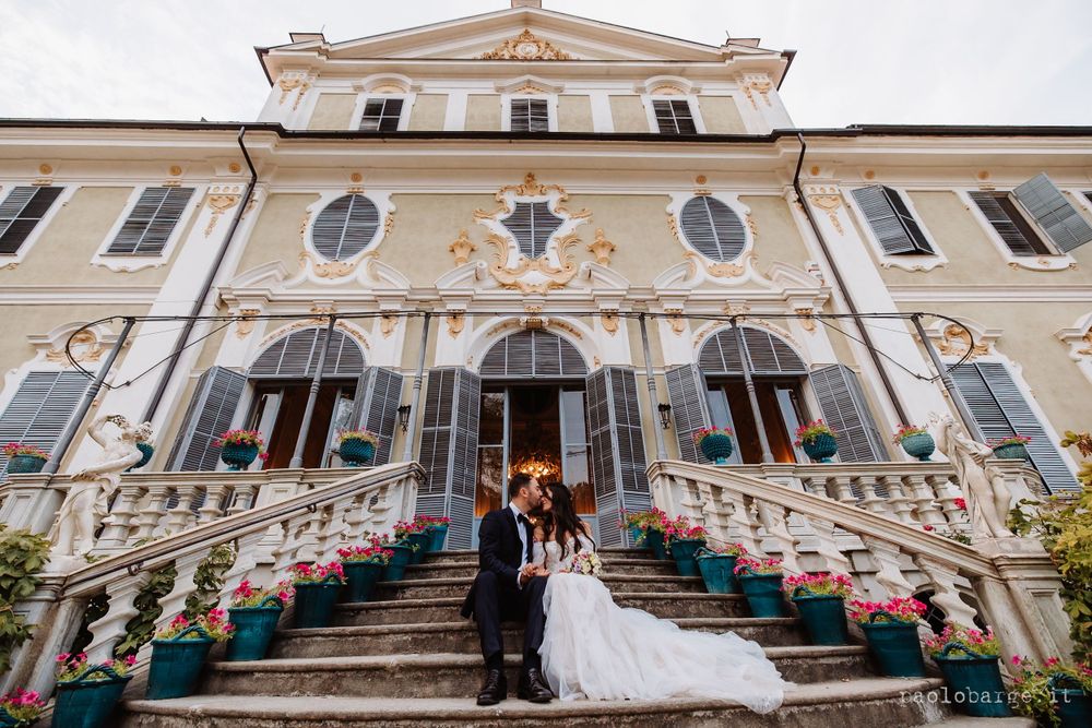 Wedding couple stands on grand staircase of ornate historic building with classical architecture.
