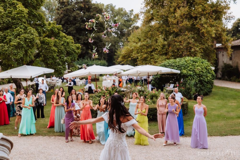 Wedding celebration in a garden with colorfully dressed guests under white umbrellas.