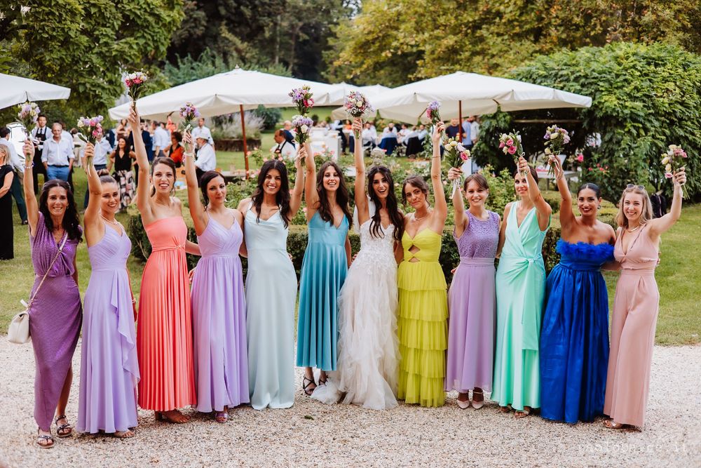 Bridesmaids in rainbow colored dresses pose together at outdoor wedding celebration.