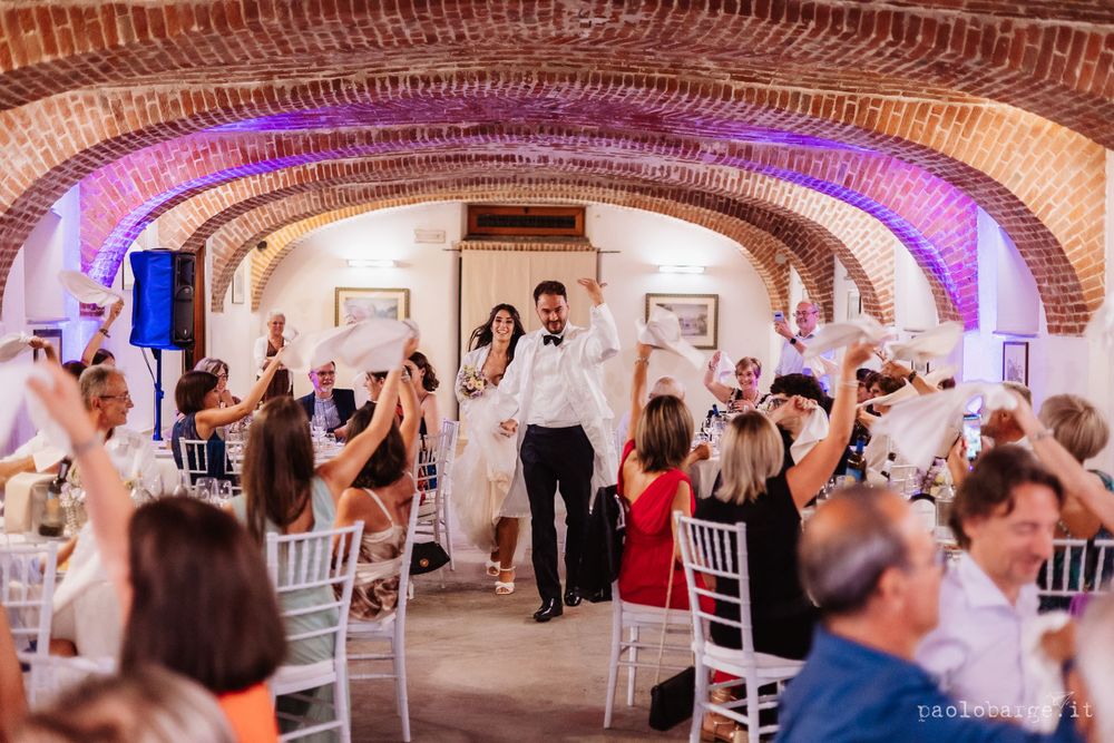 Wedding guests dancing and celebrating inside a rustic brick-arched venue with purple lighting.