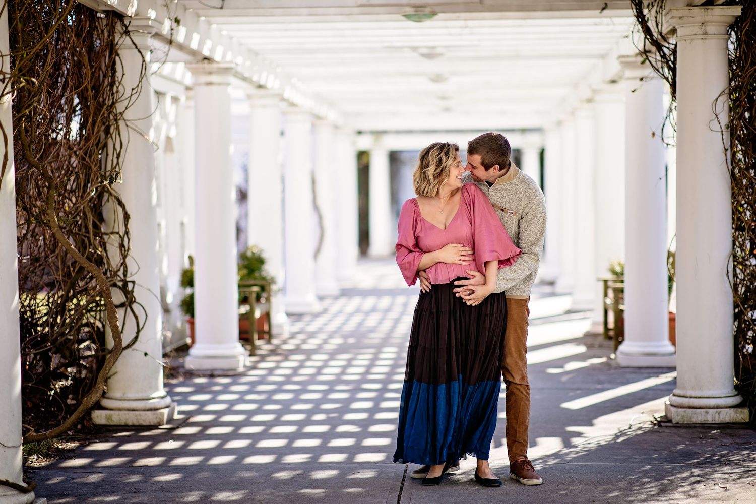 Couple embracing in romantic moment under white columned walkway.
