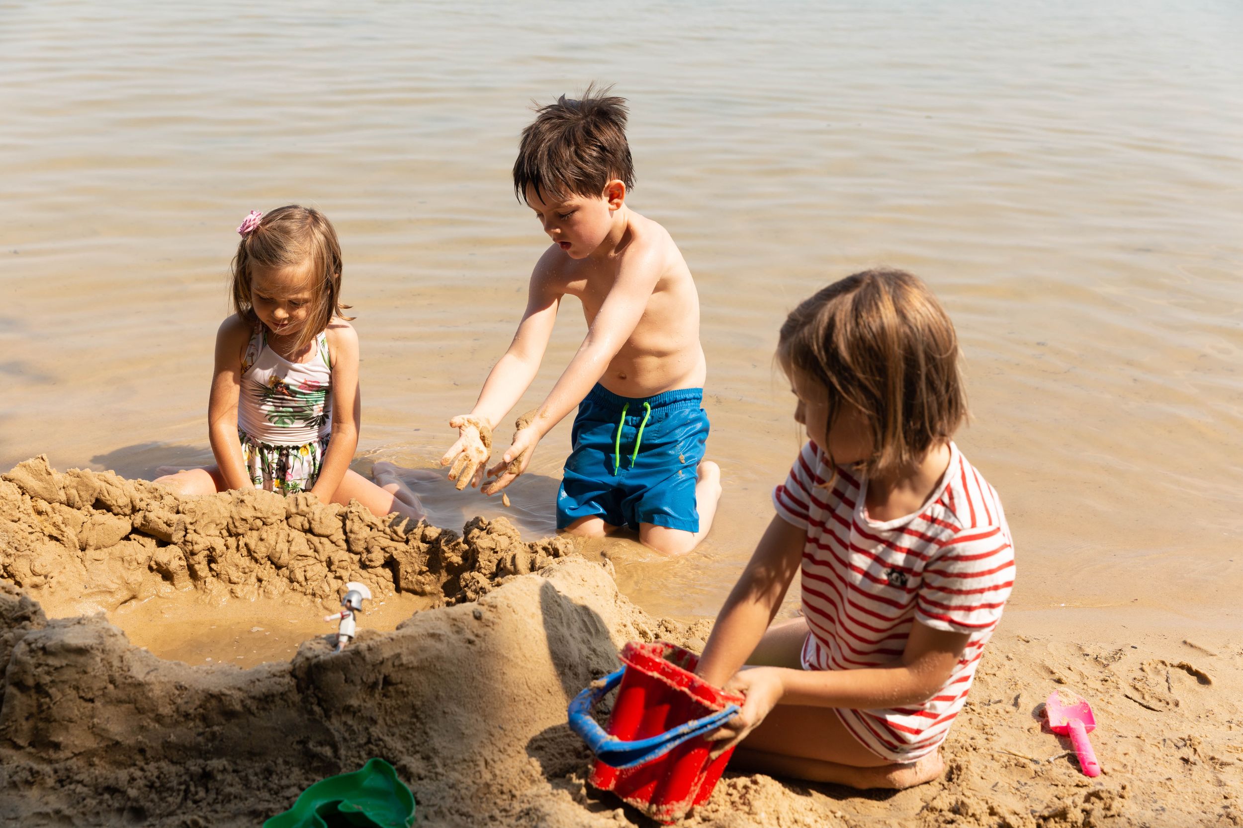 three kids building sand castle on beach
