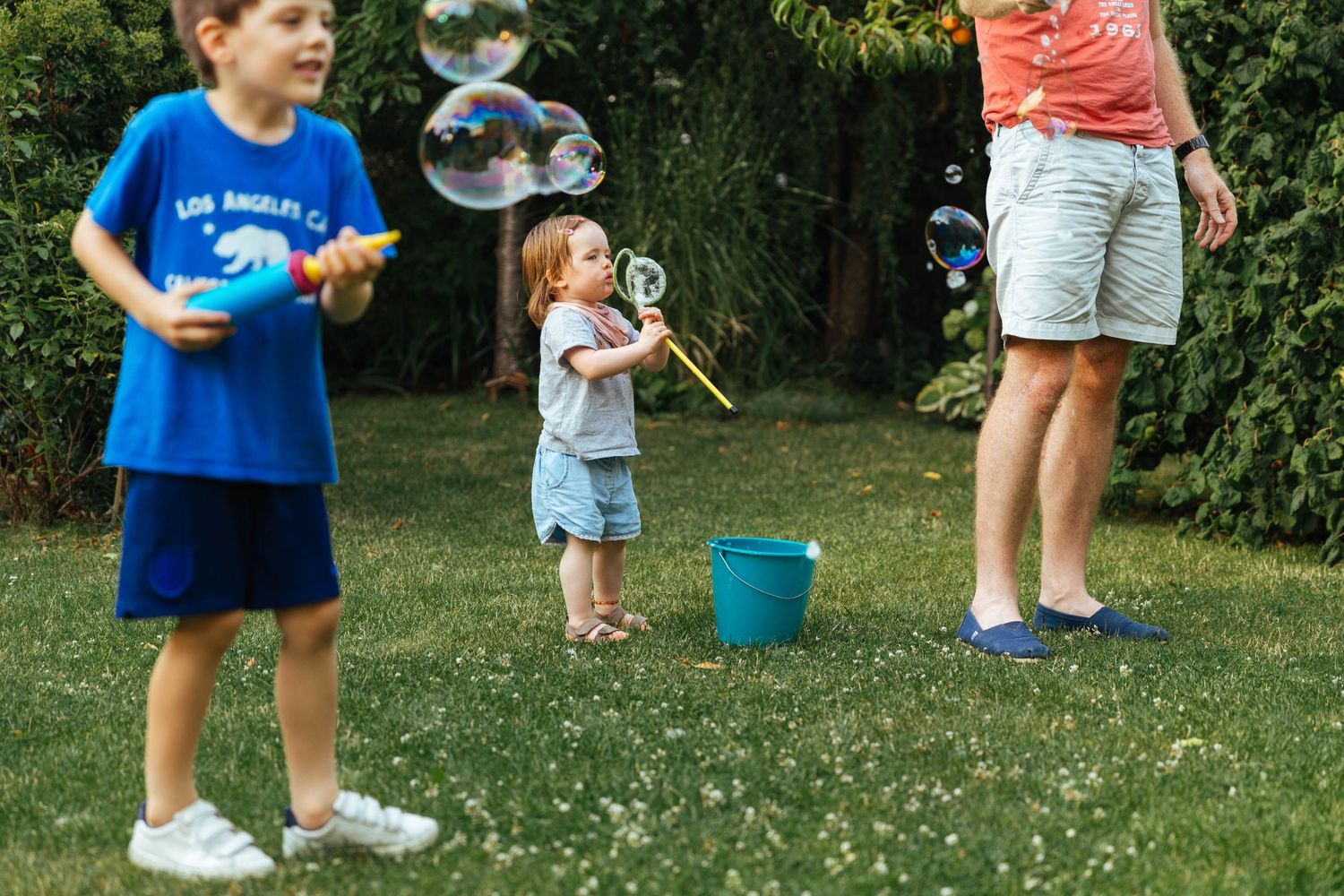 little toddler girl blowing giant bubbles in the garden