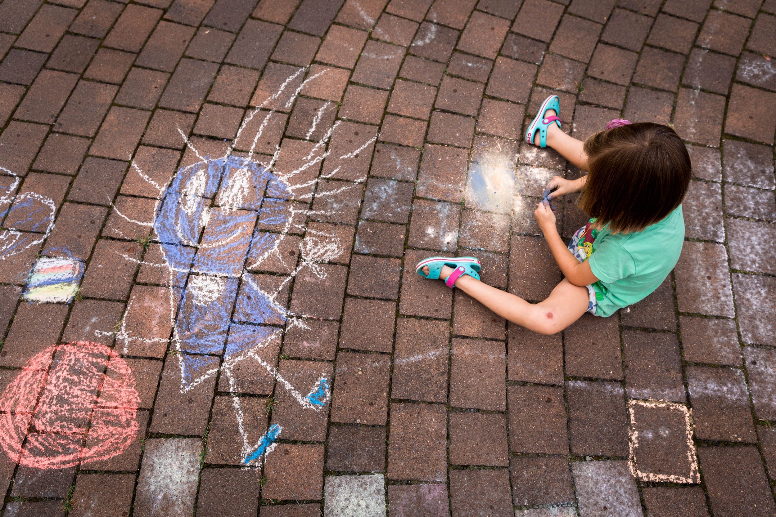 girl in green t-shirt sitting on floor drawing with chalk