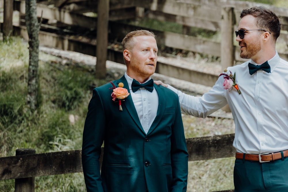 Two wedding attendants share a lighthearted moment in formal attire outdoors.