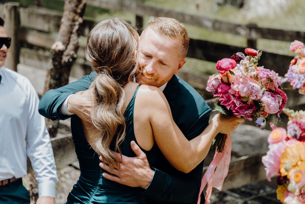 Tender embrace shared during outdoor wedding celebration with pink floral bouquets.