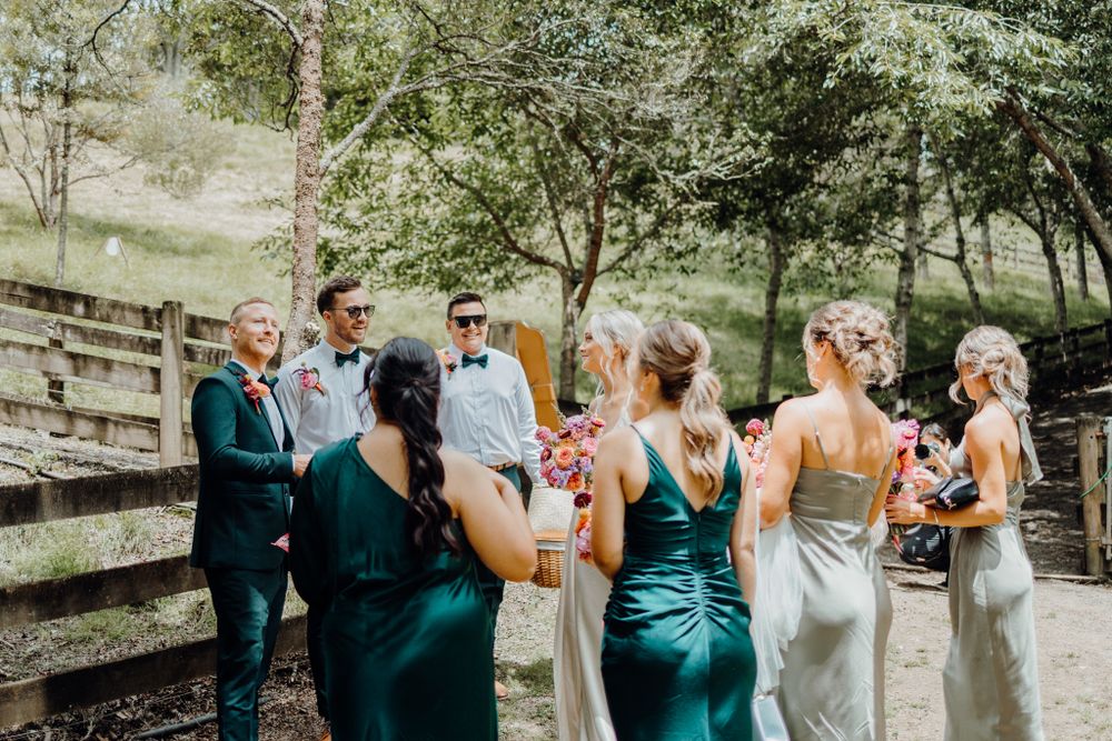 Wedding party poses together outdoors wearing teal and silver dresses holding bouquets.