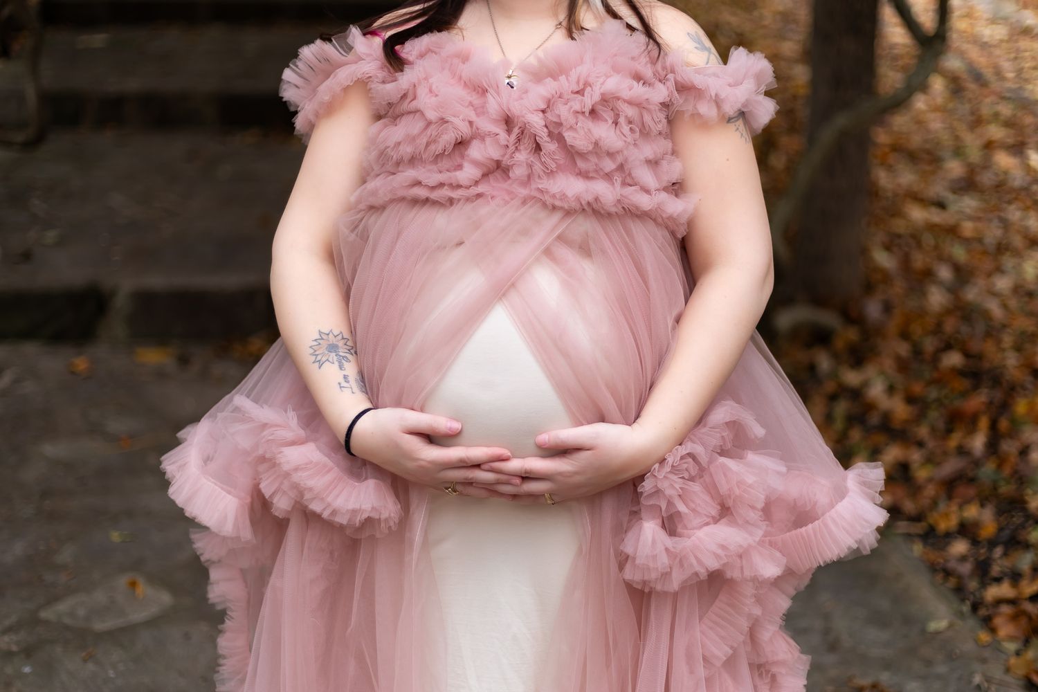 Close-up view of a pink tulle maternity dress detail against an autumn backdrop.