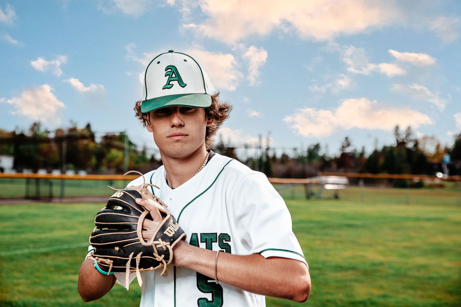 Baseball player in white uniformposes on field with glove and baseball cap.