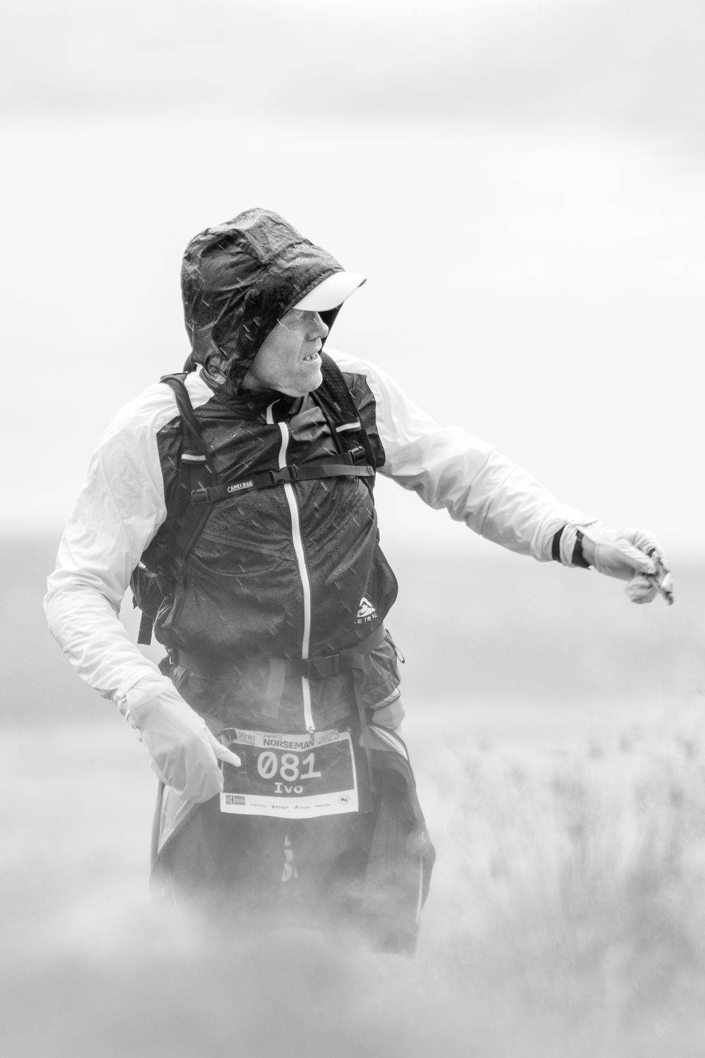 Runner in black vest and white jacket with race number 051 moves through misty terrain in black and white photograph.