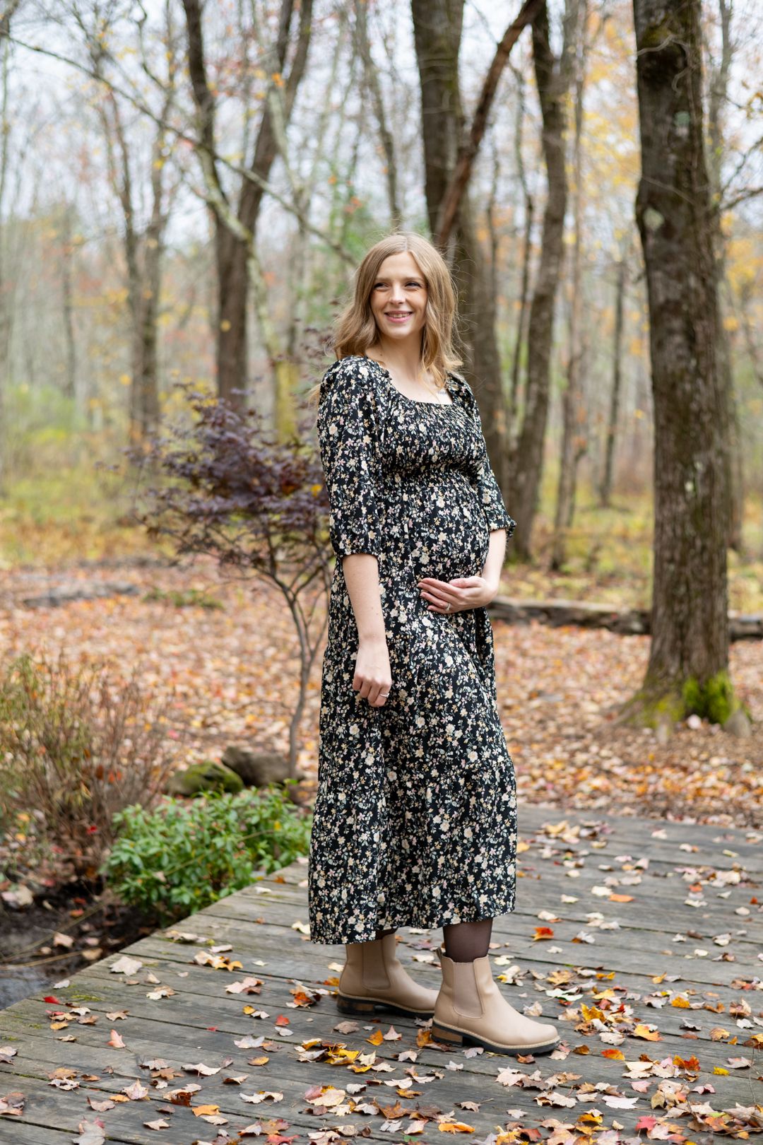 Maternity photo on wooden walkway with fall foliage in background.