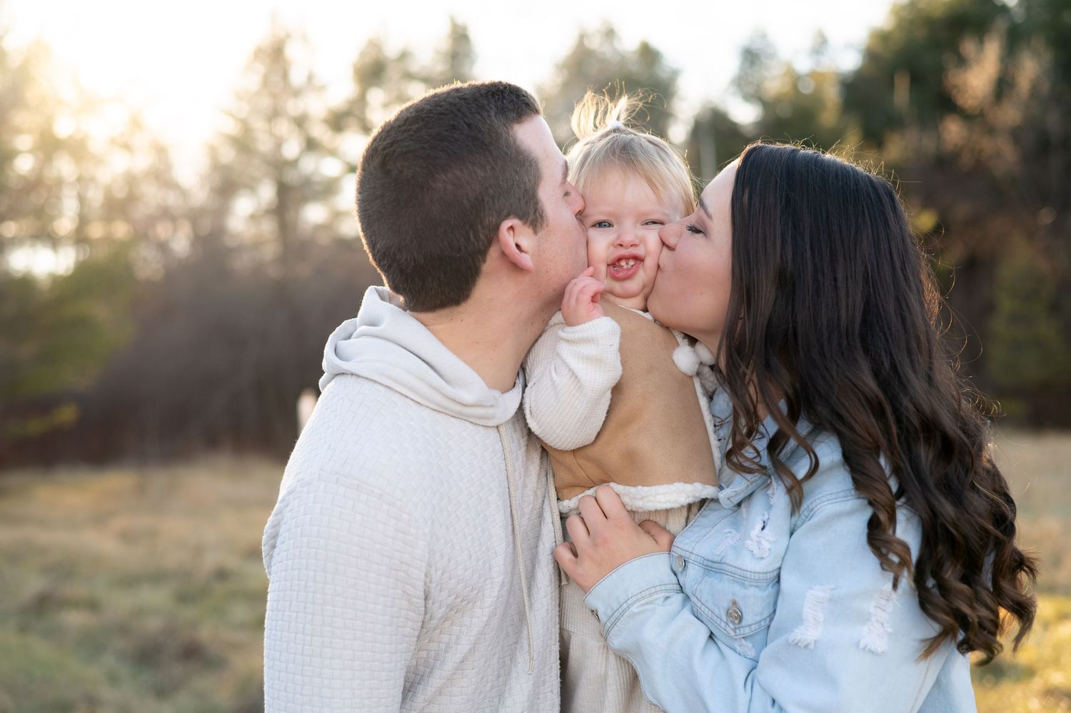 Parents sharing sweet moment with child in outdoor setting at sunset.