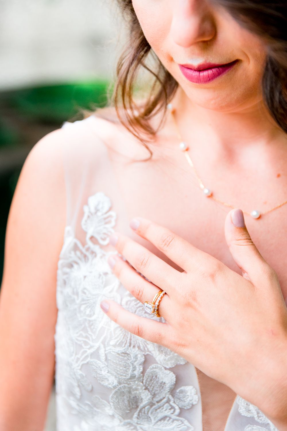details of bride's lipstick, wedding dress, necklace, and engagement and wedding rings