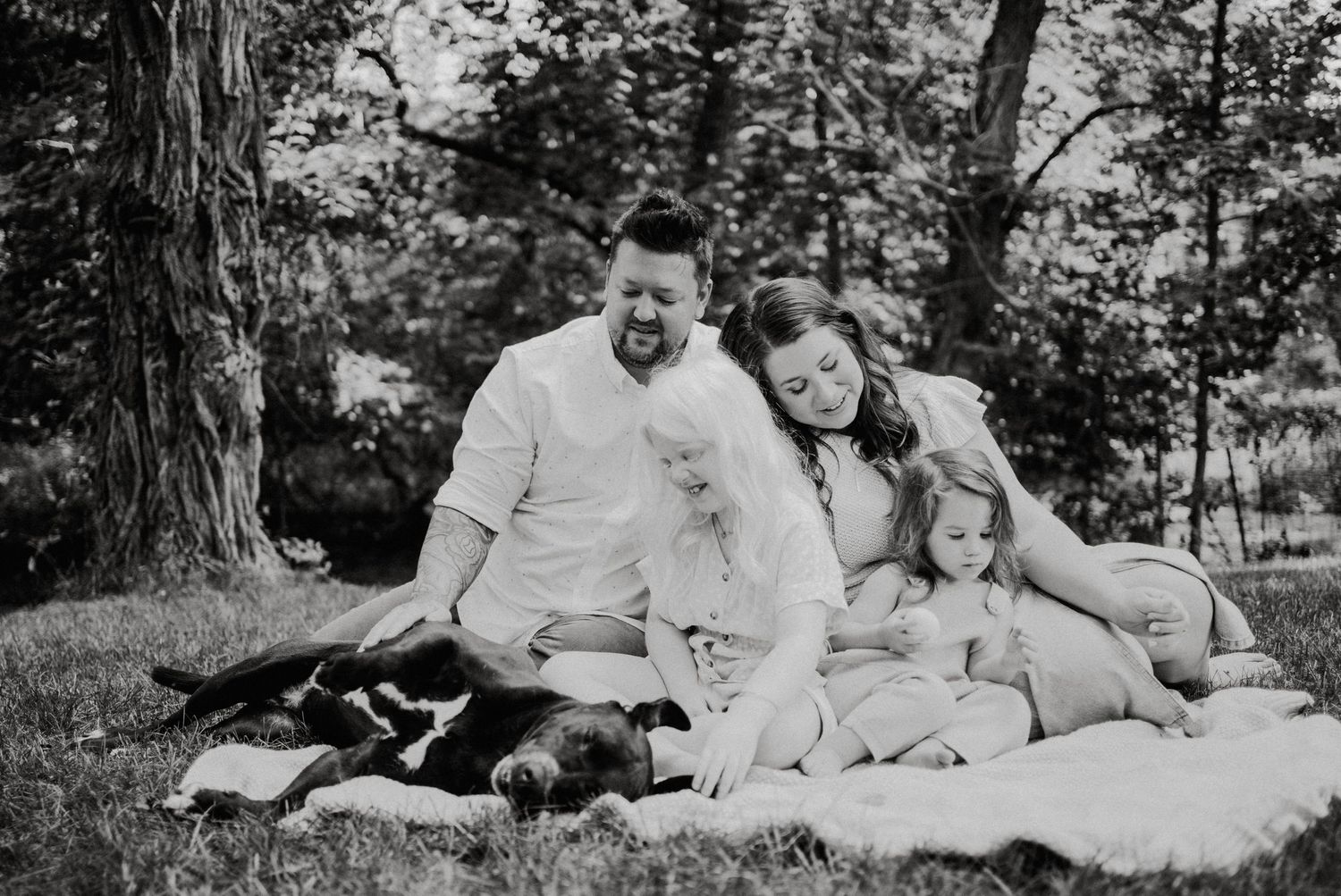 Family photoshoot on a grassy lawn surrounded by trees in black and white.