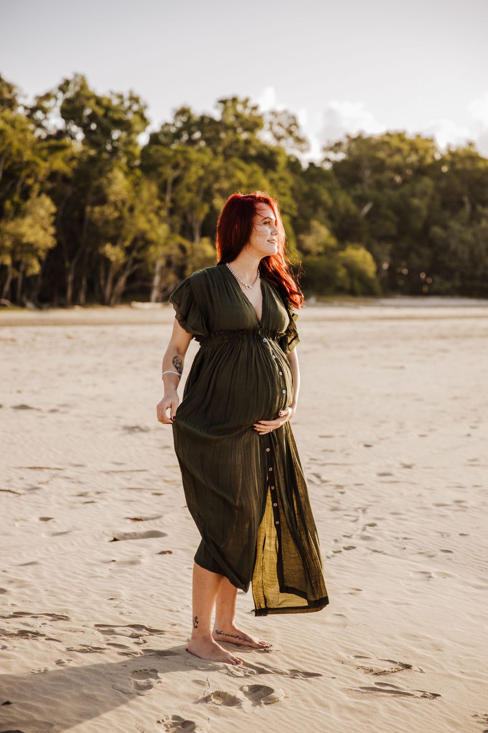 beautiful pregnant lady with bright red hair showing off her bump at the beach for a photoshoot