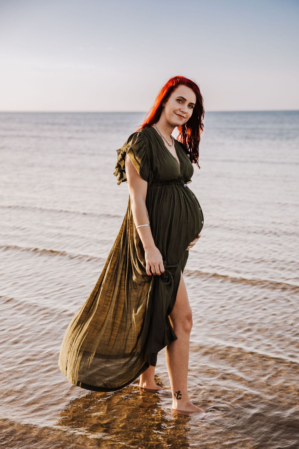 beautiful pregnant pregnant lady with bright red hair on the beach showing off her bump at the beach for a photoshoot