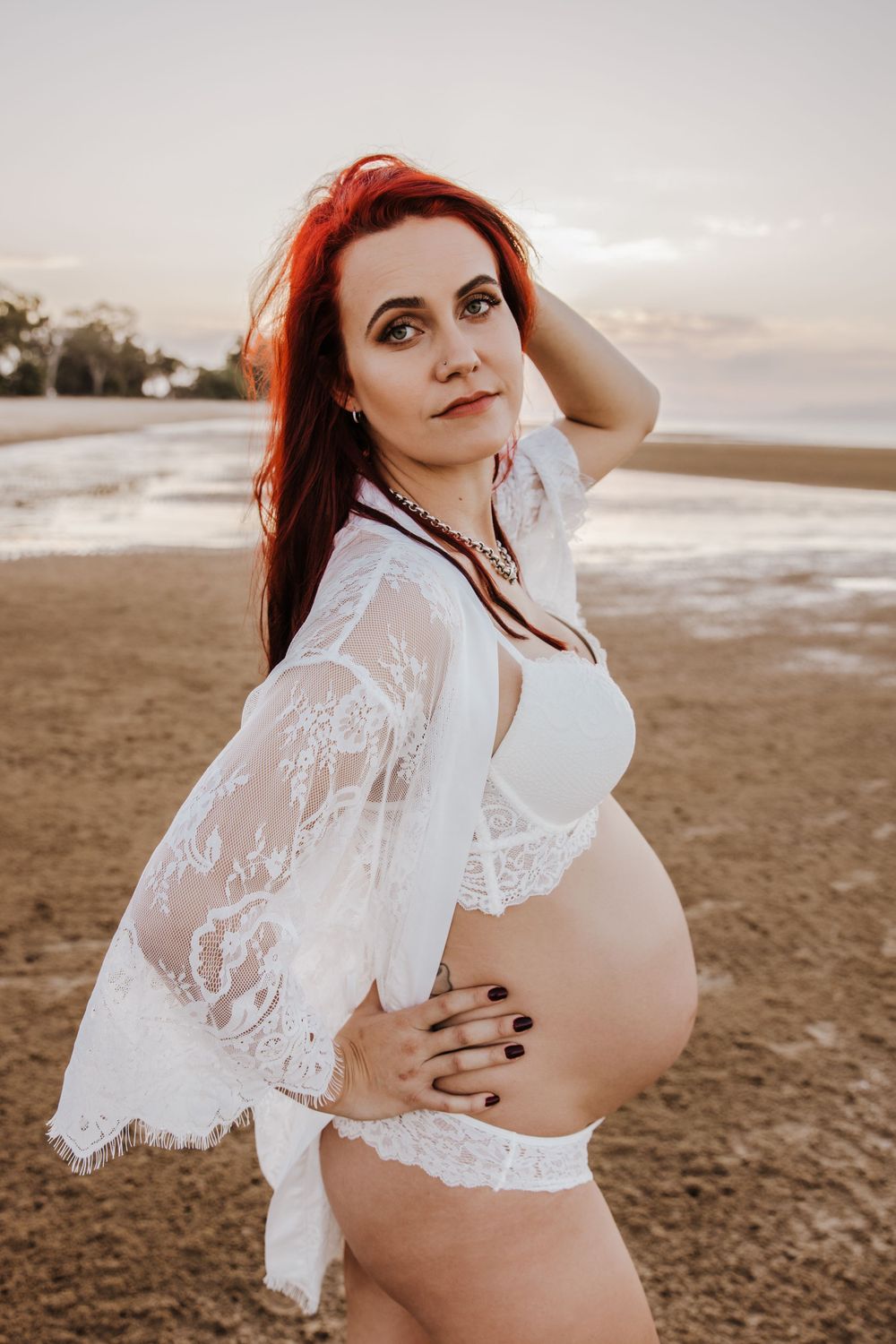 beautiful pregnant pregnant lady with bright red hair on the beach showing off her bump at the beach for a photoshoot