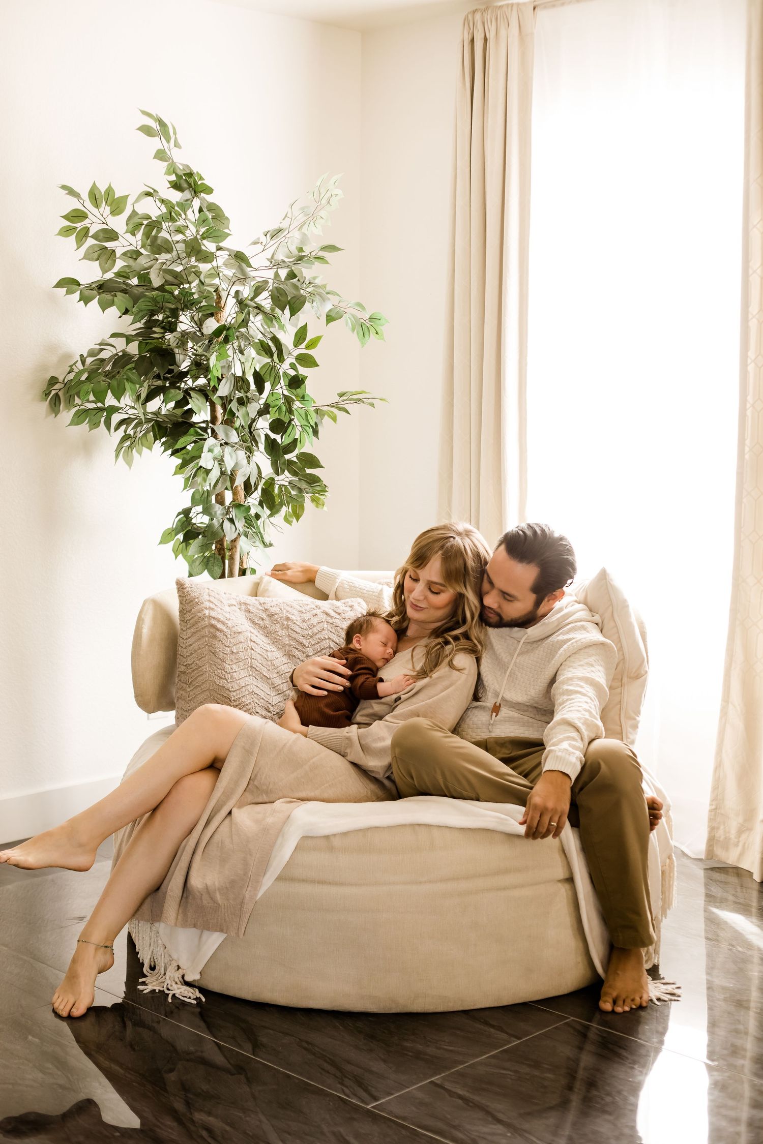 An in home lifestyle portrait of mom and dad on the couch snuggling their newborn baby.
