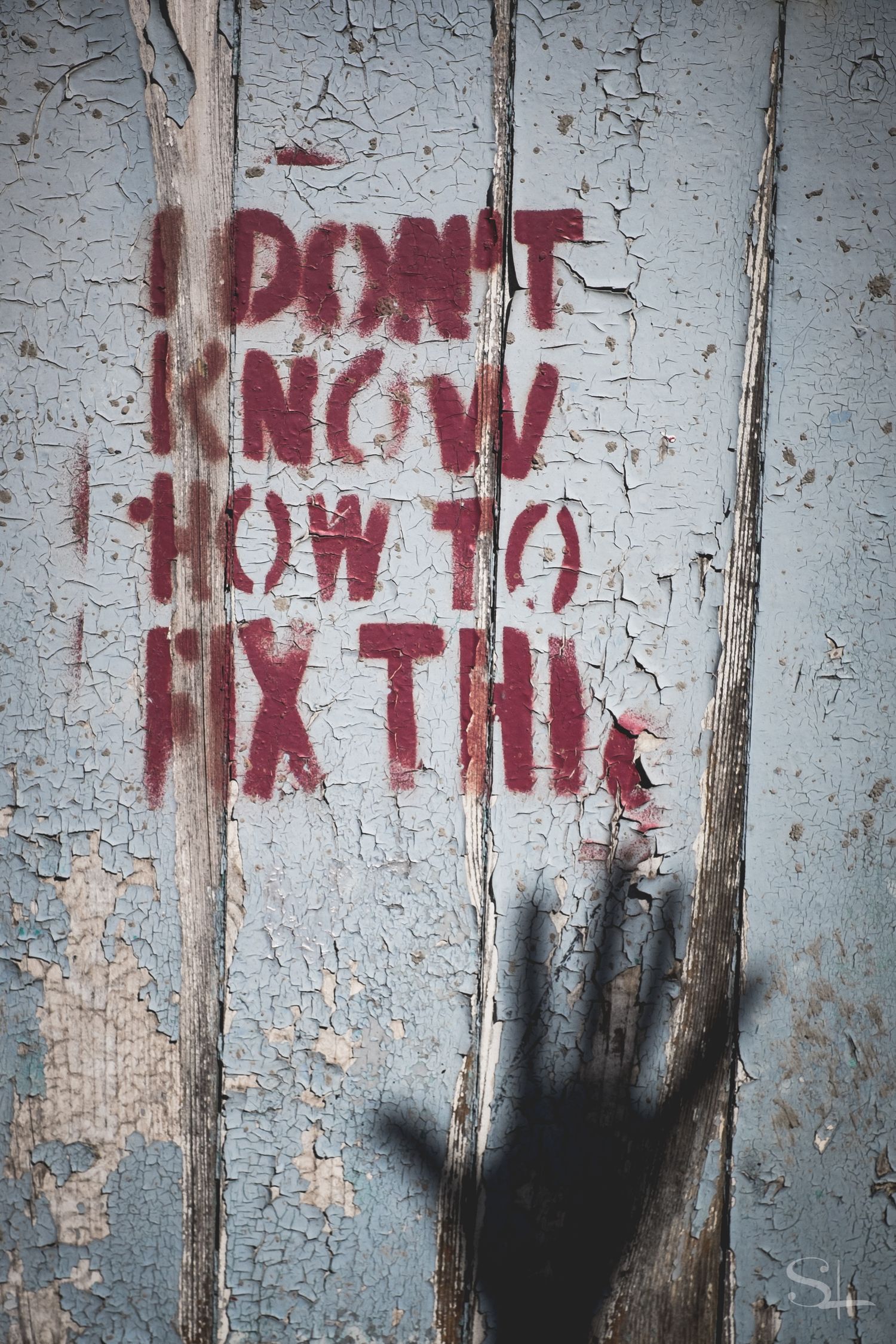 red stencilled words "I don't know how to fix this" on blue chipping paint with a shadow of a open hand at the bottom