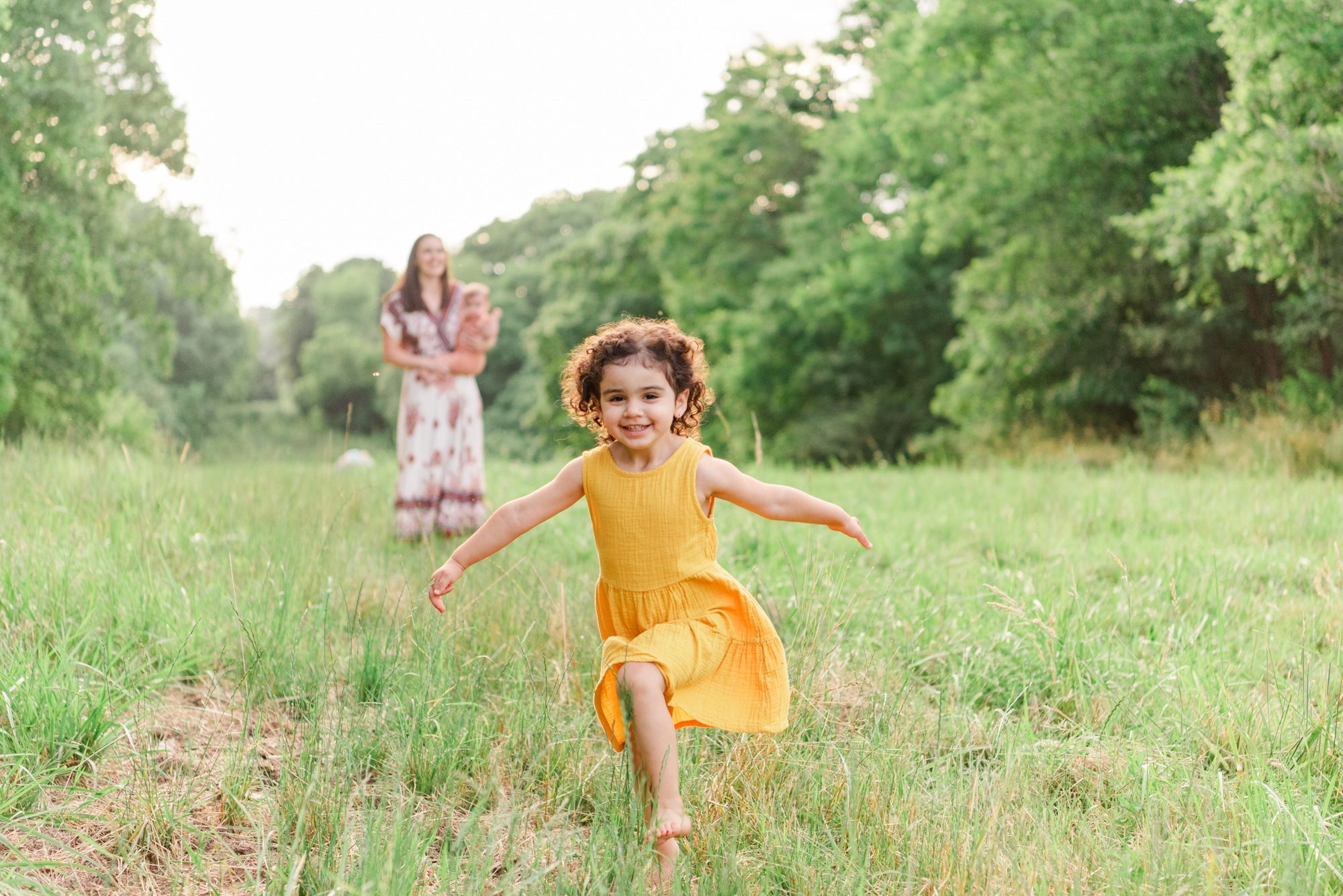 Little girl running through field with family in background in Pittsburgh, Pennsylvania