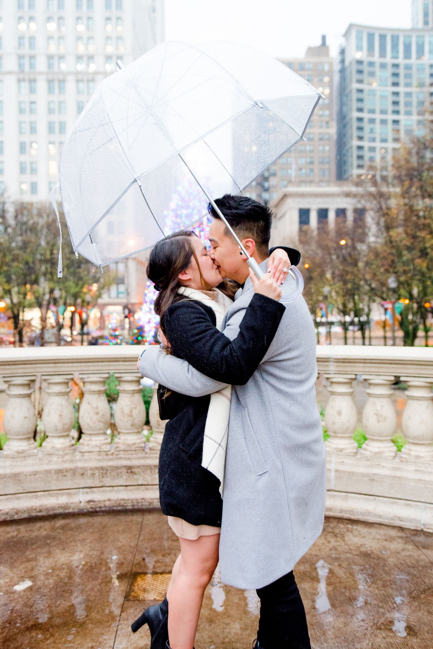 couple hugging under clear umbrella in front of Millennium Park Christmas Tree