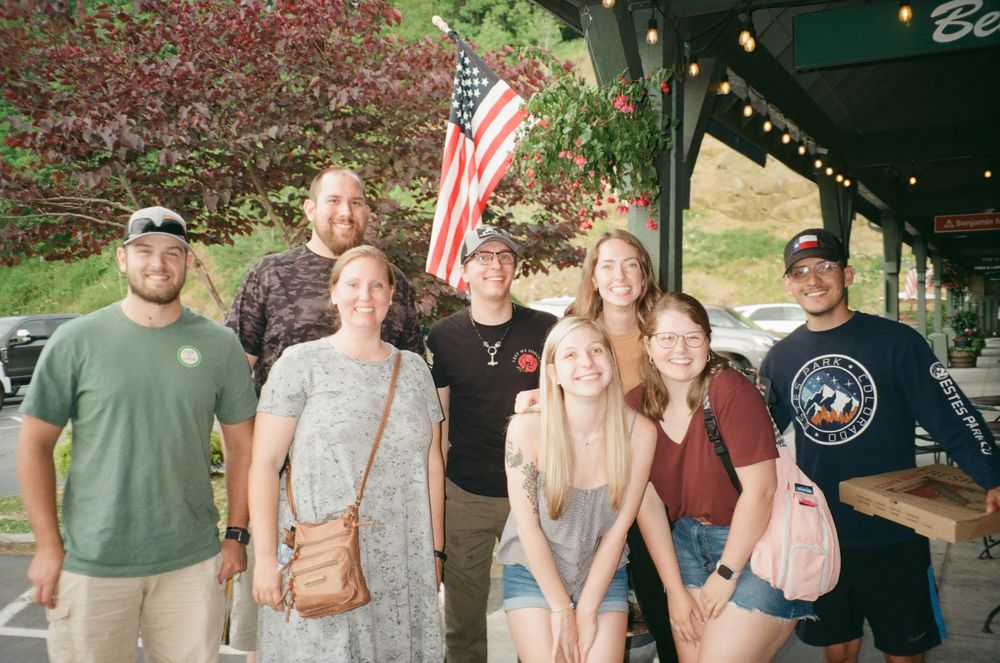 Group photo of friends gathered outside with American flag in background.