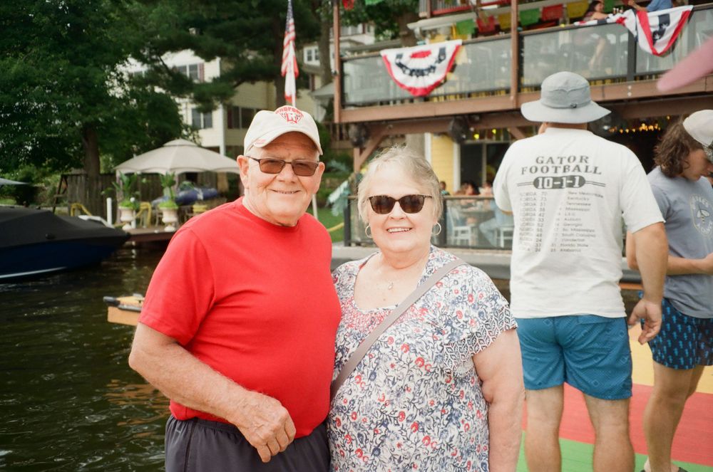 Couple in casual attire standing together at waterfront with patriotic decorations.