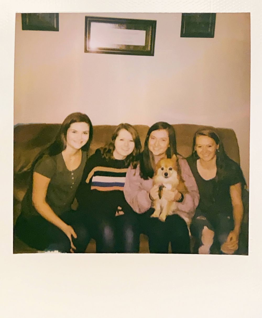 Polaroid style photo of friends relaxing on couch with small dog.