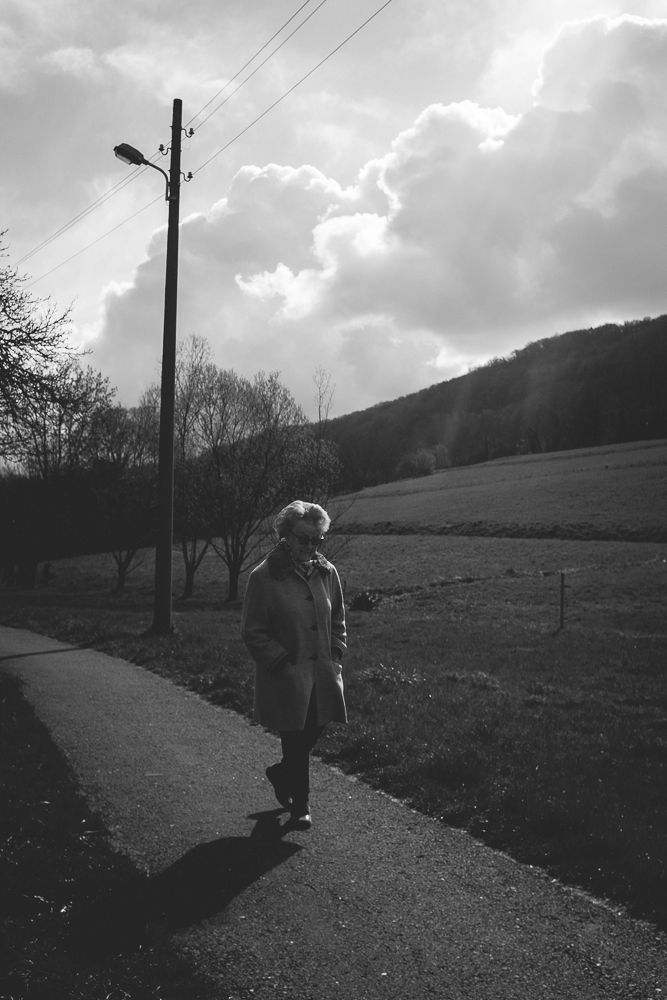 Figure walking along path under dramatic clouds and utility pole in countryside setting.