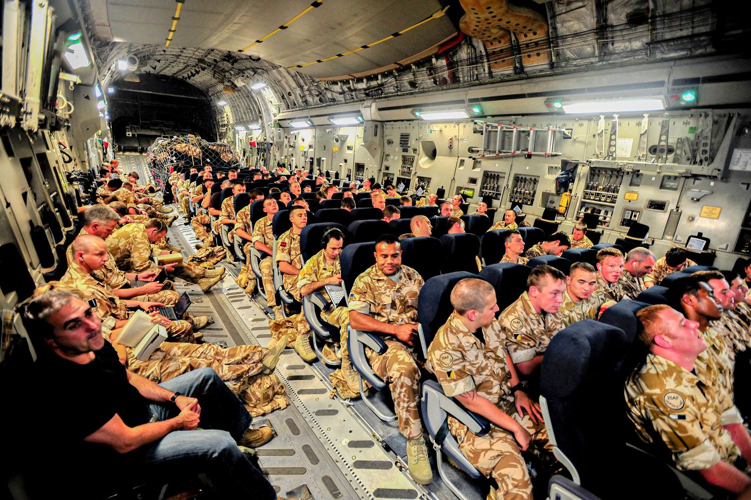 Military personnel seated in rows inside large transport aircraft during meal service.