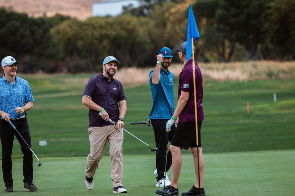 Golfers stand on putting green with flag markers during afternoon game.