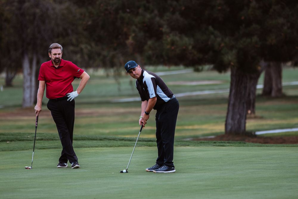 Two golfers line up their putts on the green at dusk.
