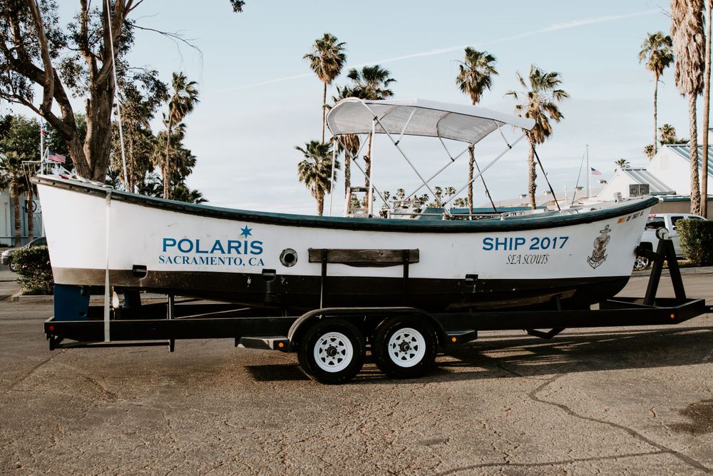 White Polaris fishing boat on trailer parked near palm trees.