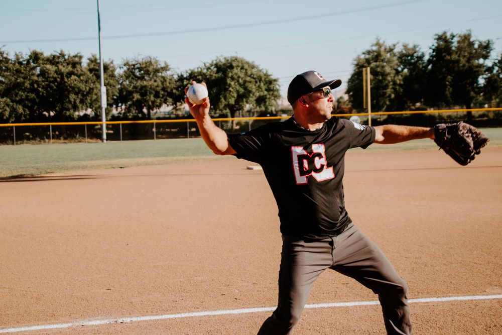 Baseball player in gray uniform throws pitch on dirt infield.