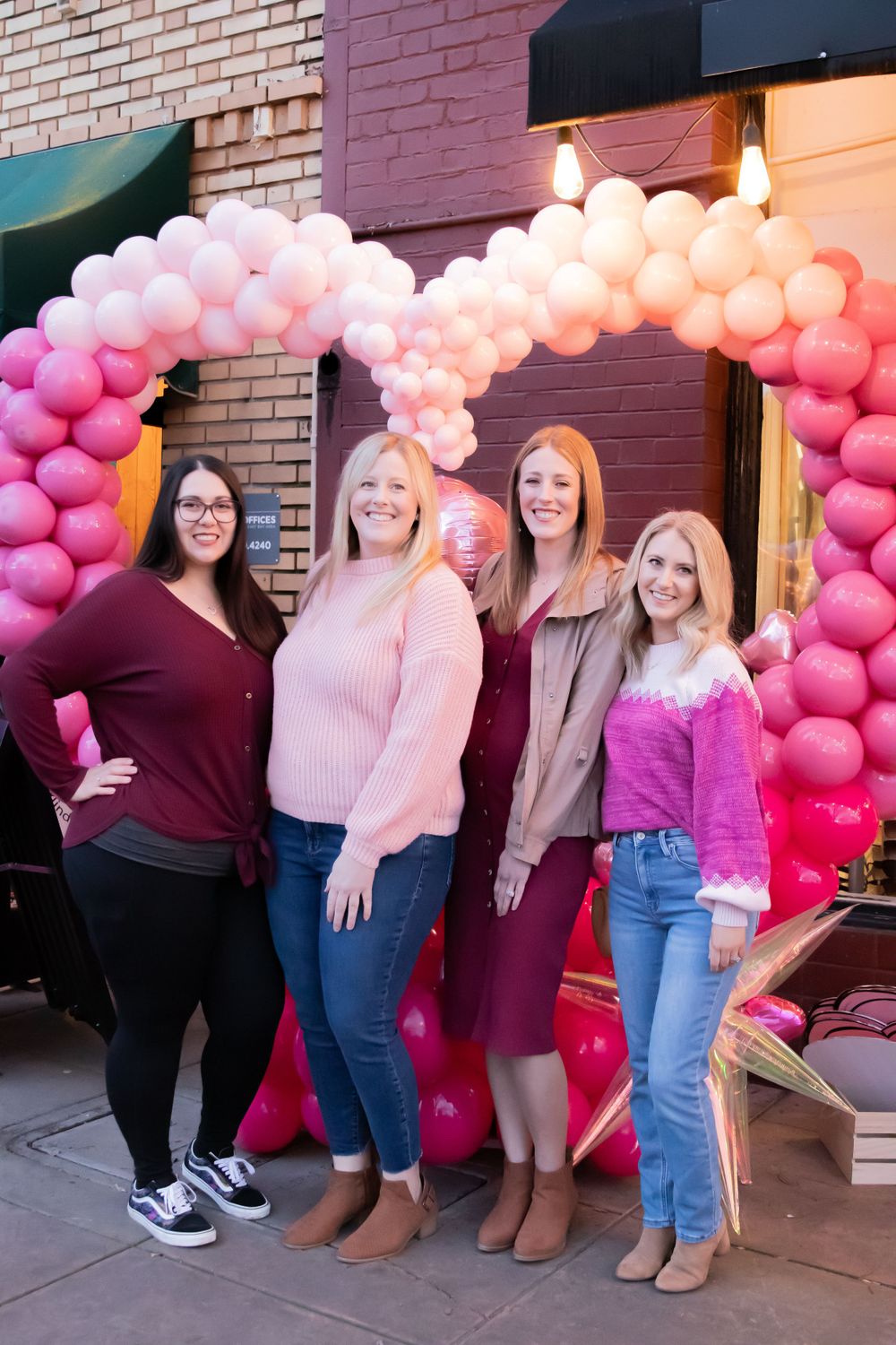 Group stands together under a pink balloon arch during a special event.