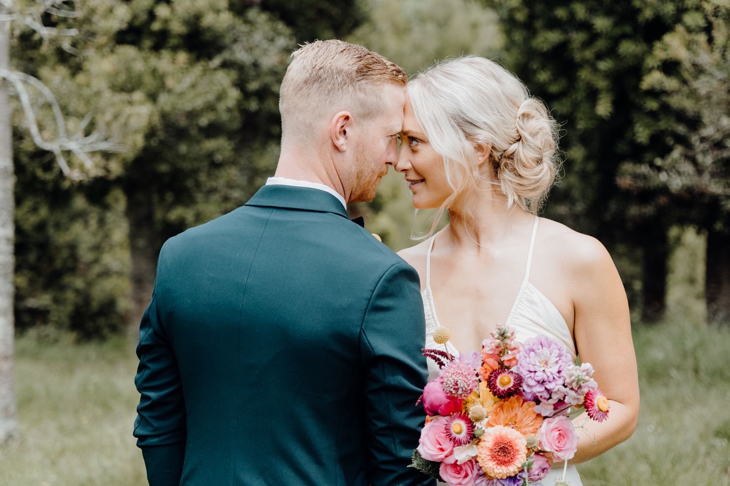 Romantic wedding portrait with emerald suit and pink floral bouquet in outdoor garden setting.