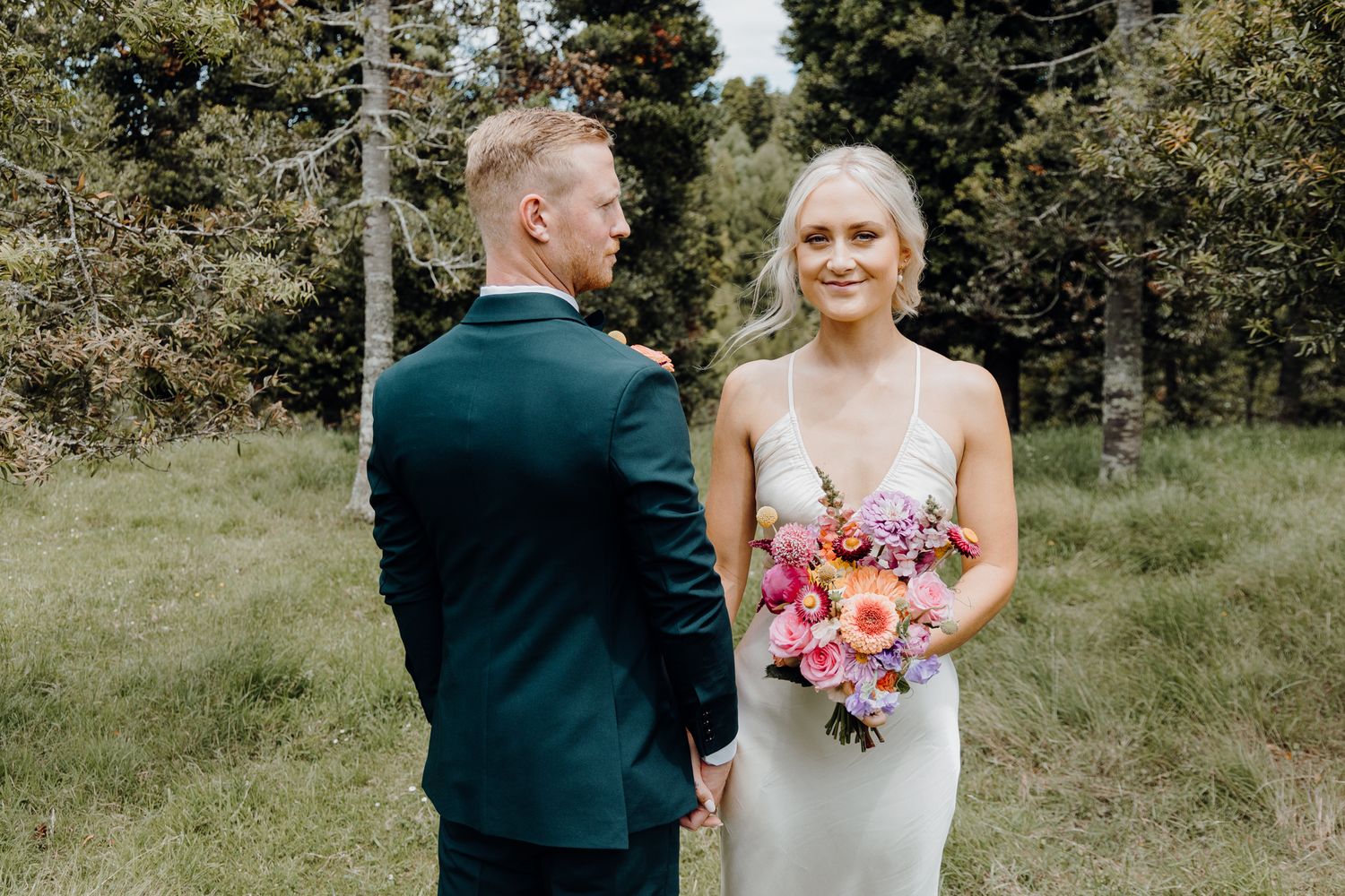 Wedding couple in forest with emerald suit and pink bouquet.