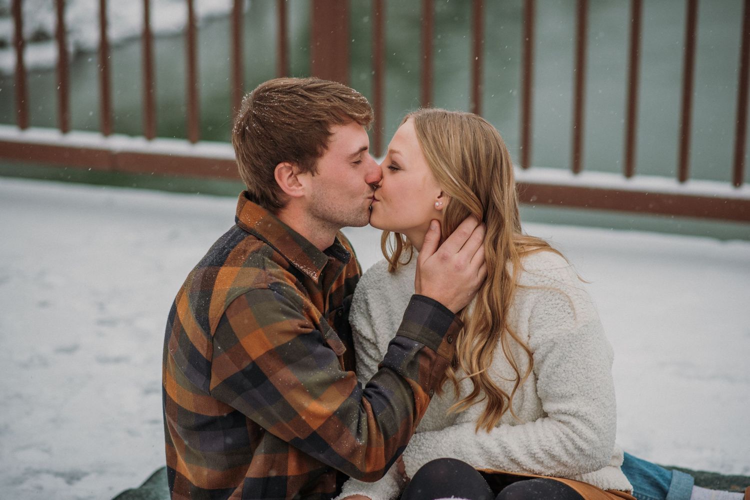 couple kissing on the snow, sitting on snowy bridge on Pendleton blanket, west glacier Montana