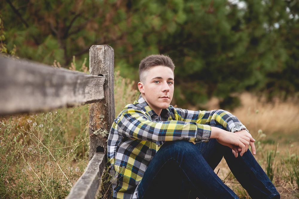 senior boy sitting on the ground and leaning against a fence