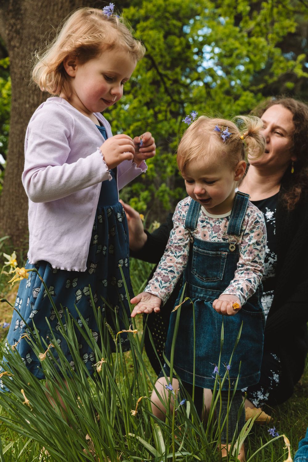 Children explore springtime flowers and grass in a garden while wearing cute overalls and cardigans.