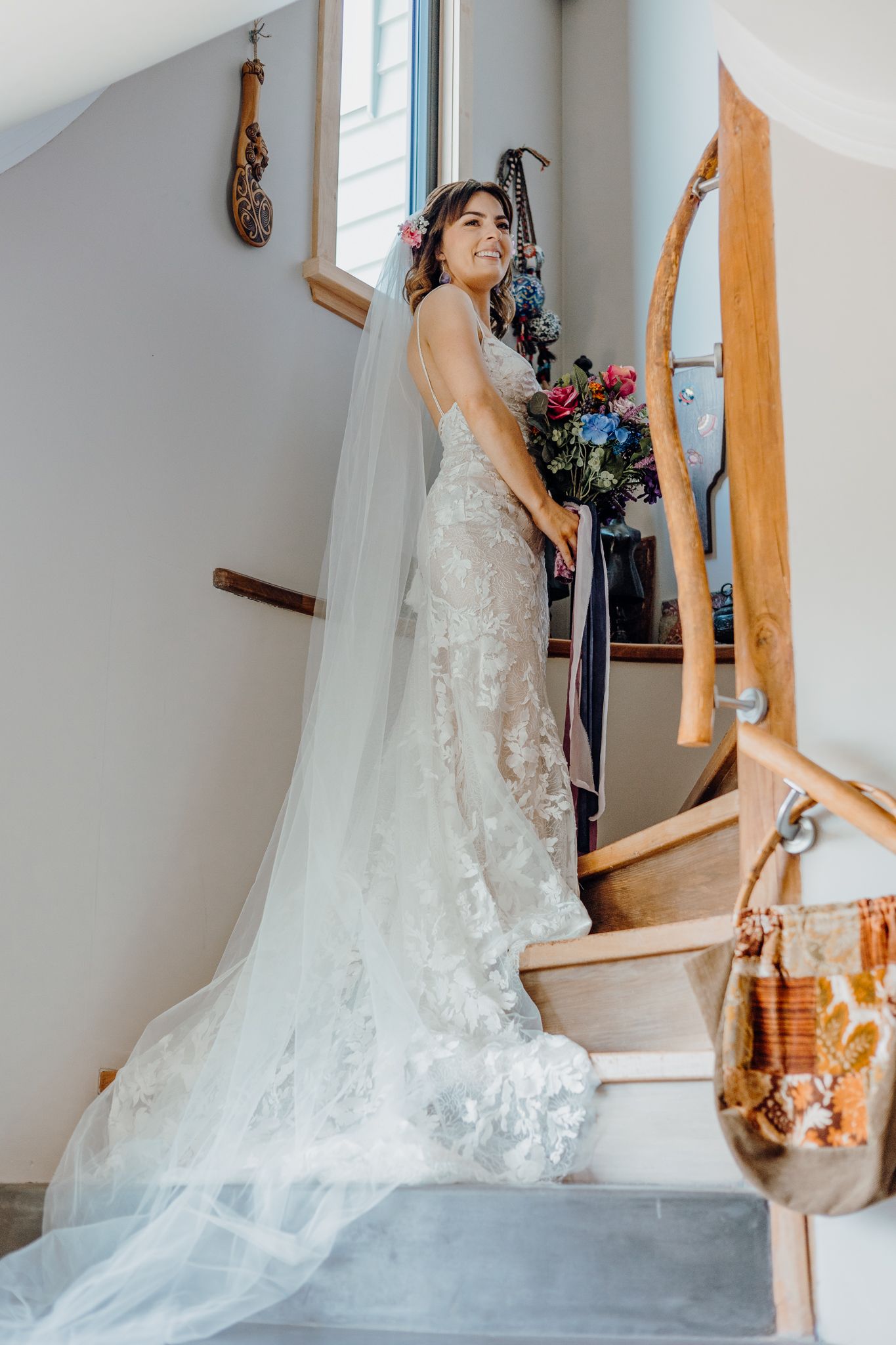 An elegant bridal portrait on a white staircase with flowing lace dress and floral bouquet.